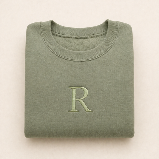 Folded green sweatshirt with a large 'R' on a beige background