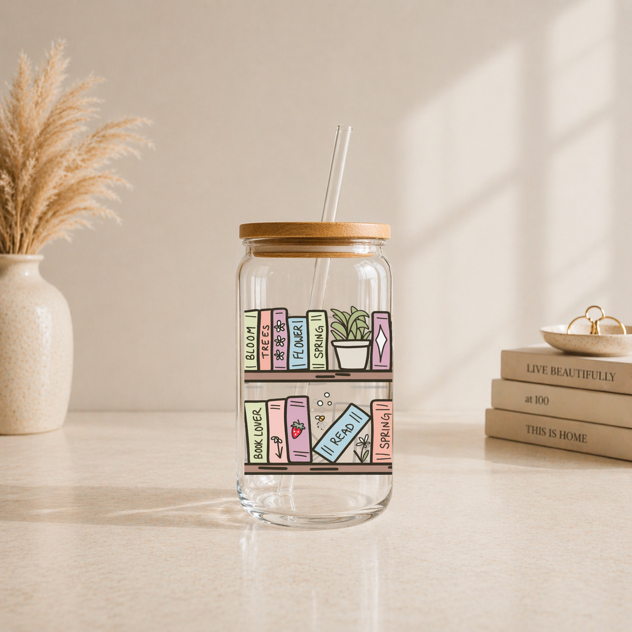 glass iced coffee cup with illustrated bookshelf and pastel books design on neutral aesthetic background with bamboo lid and glass straw