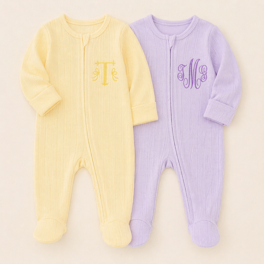 Two baby footie pajamas, one yellow and one purple, with monograms on a beige background.