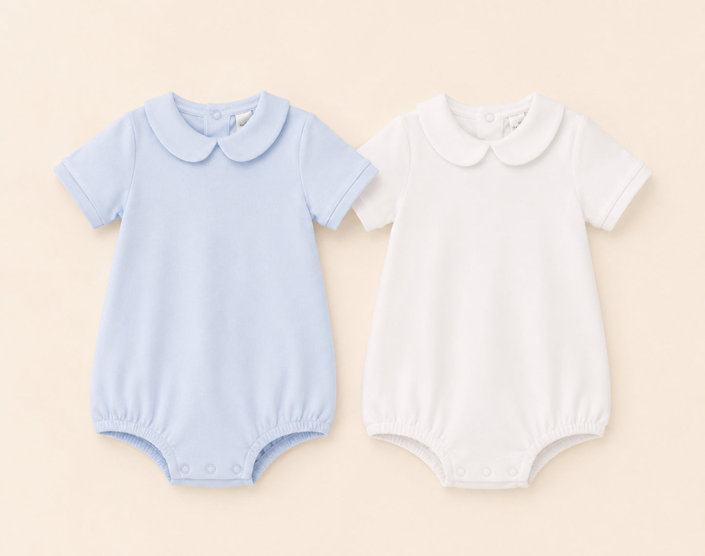 Two Peter Pan baby rompers, one blue and one white, on a beige background