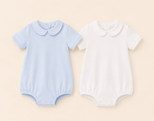 Two Peter Pan baby rompers, one blue and one white, on a beige background