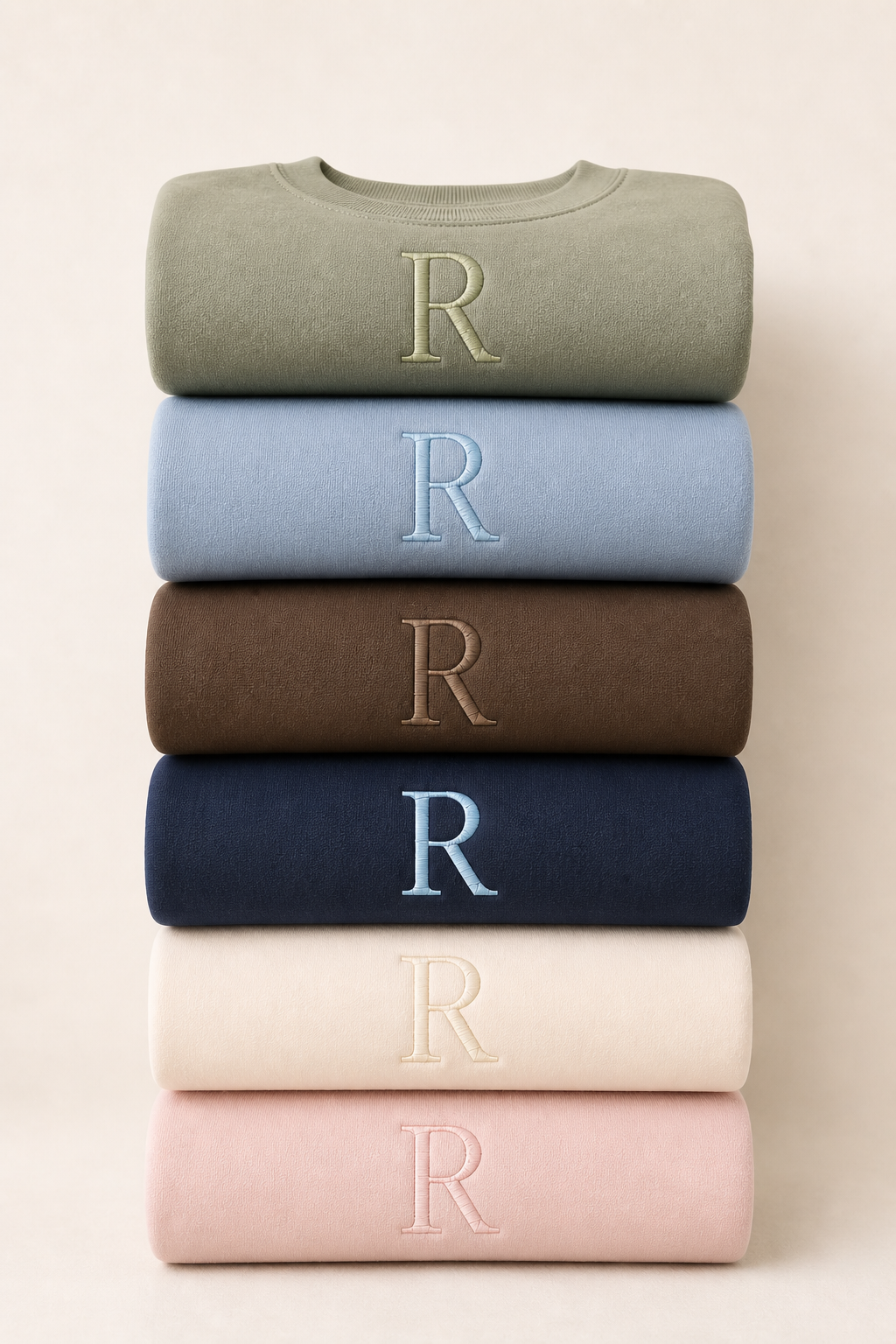 Stack of six sweatshirts with 'R' logo in various colors on a beige background