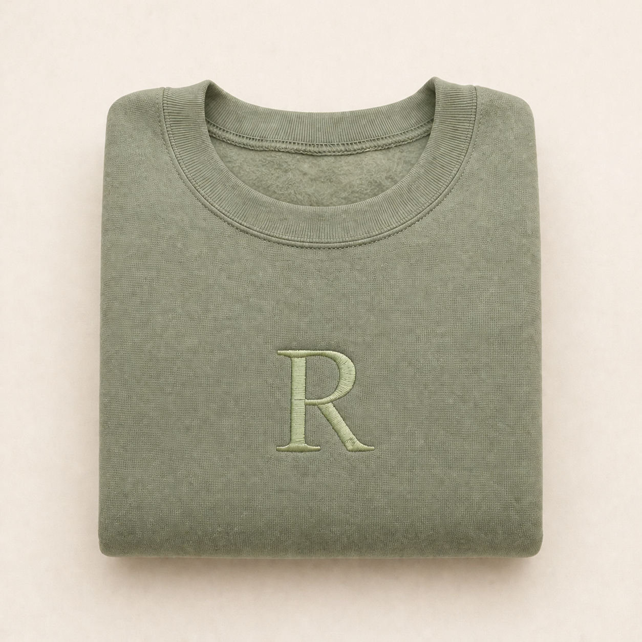Folded green sweatshirt with a large 'R' on a beige background