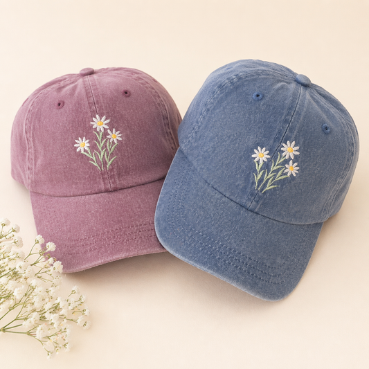 Two baseball caps, one purple and one blue, with floral embroidery on a beige background.