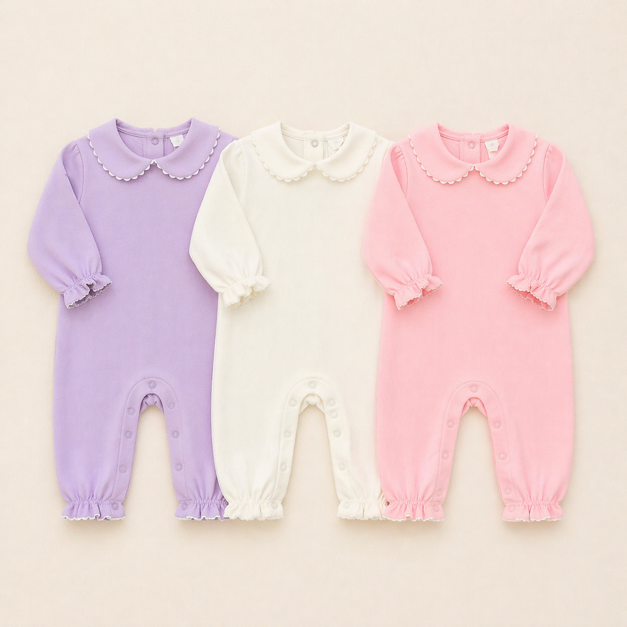 Three baby rompers in purple, white, and pink on a beige background