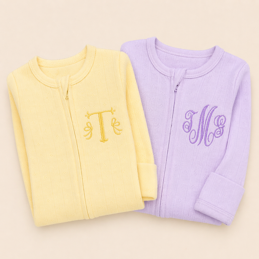 Yellow and purple baby rompers with embroidered initials on a beige background