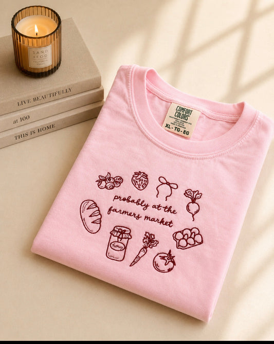 Pink Comfort Colors embroidered t-shirt featuring “Probably At The Farmers Market” design with market-inspired icons including strawberries, bread, carrots, honey, and vegetables.
