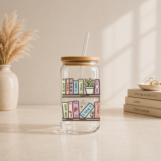 glass iced coffee cup with illustrated bookshelf and pastel books design on neutral aesthetic background with bamboo lid and glass straw