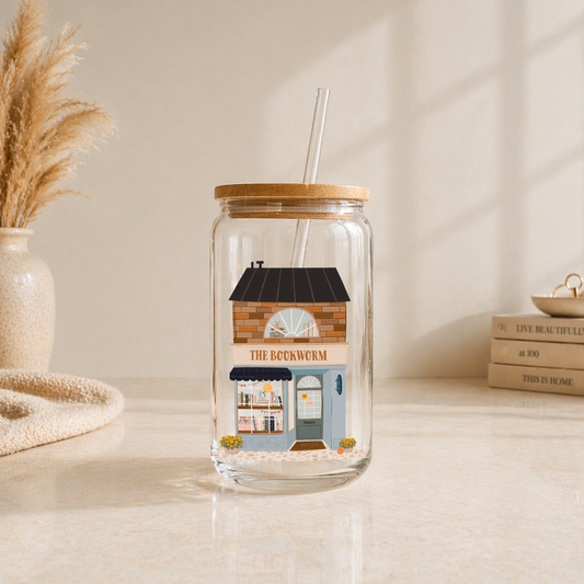 glass iced coffee cup with illustrated bookshop storefront design on neutral aesthetic background with bamboo lid and glass straw