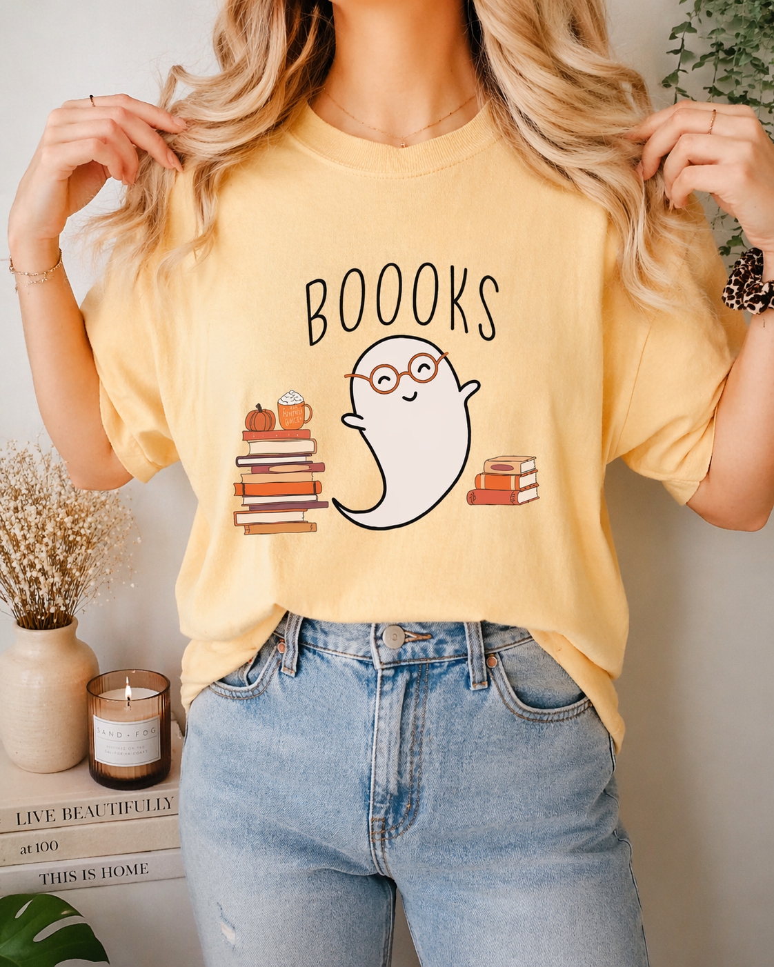 Person wearing a yellow t-shirt with a ghost and book design, standing in a room with decor.