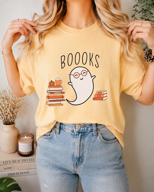 Person wearing a yellow t-shirt with a ghost and book design, standing in a room with decor.