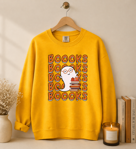 Yellow sweatshirt with 'BOOKS' text design on a hanger against a beige wall.