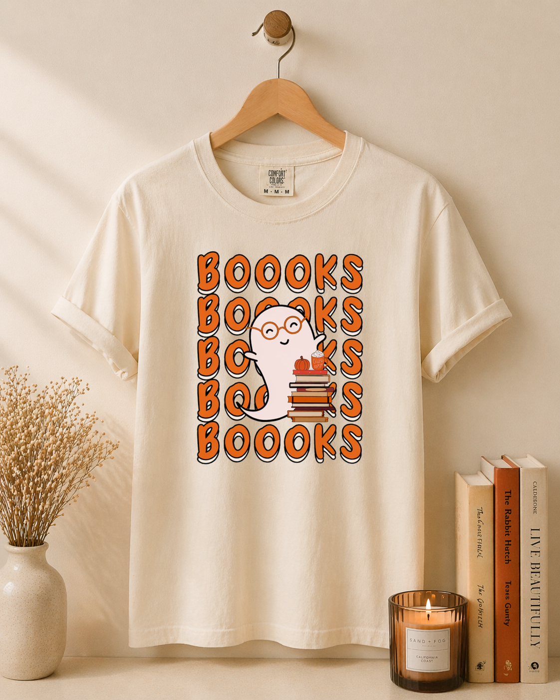 White t-shirt with 'BOOOKS' design on a wooden hanger against a beige wall.