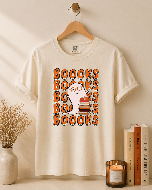 White t-shirt with 'BOOOKS' design on a wooden hanger against a beige wall.