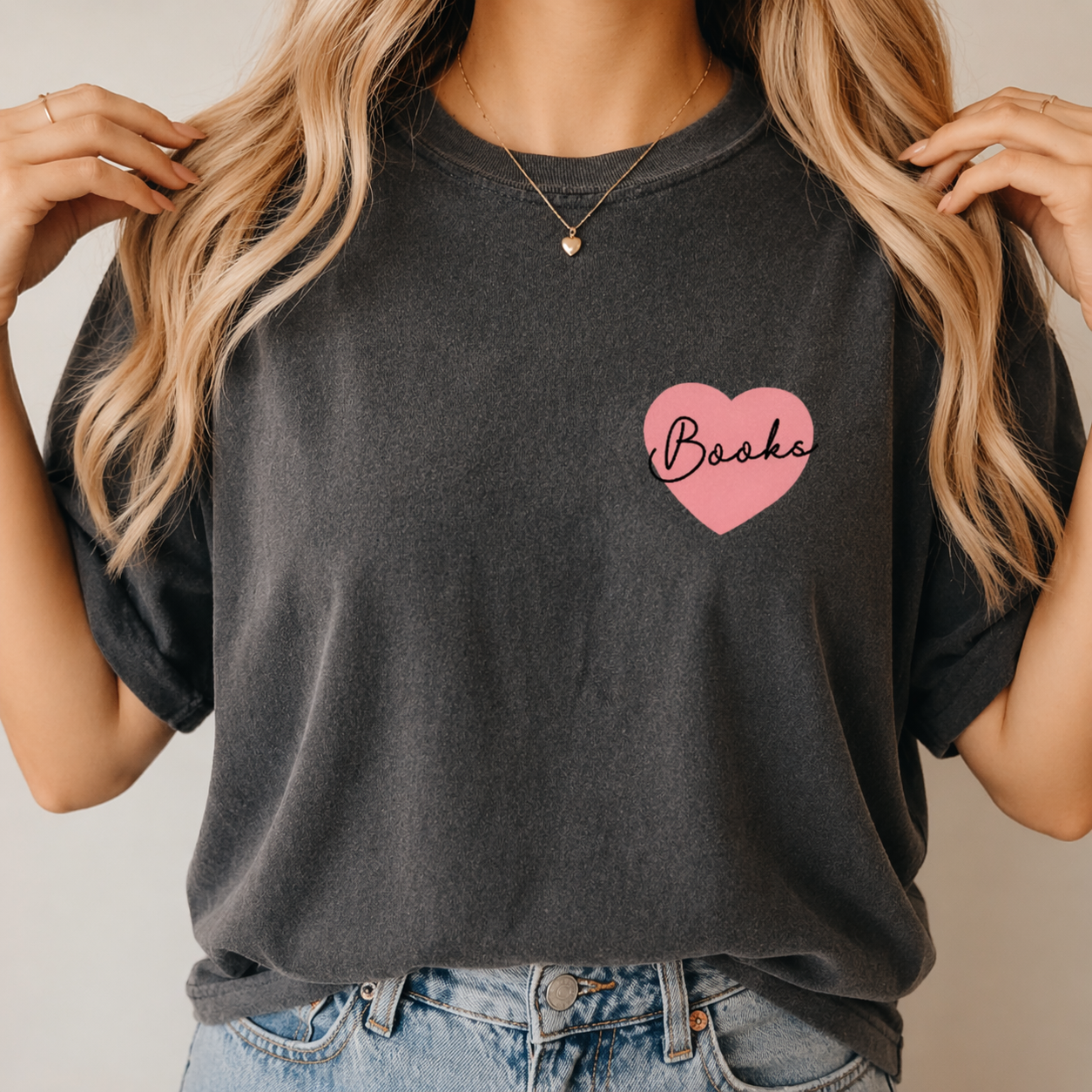 Person wearing a dark gray t-shirt with a pink heart and 'Books' text, paired with blue jeans.