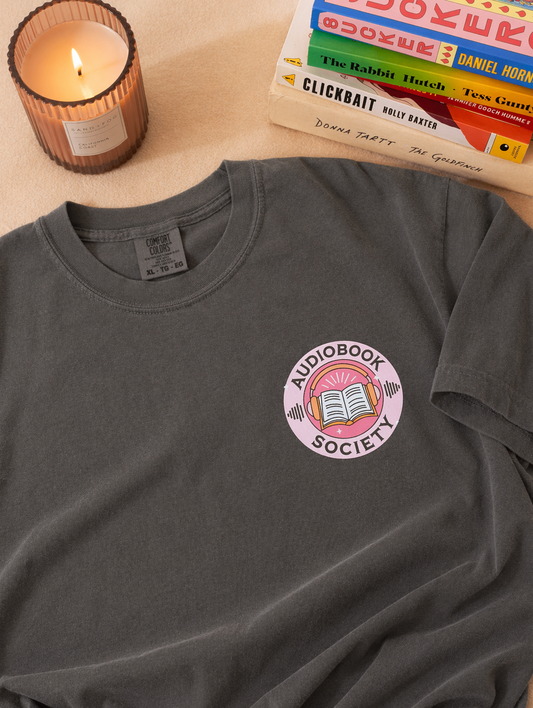 Gray t-shirt with small “Audiobook Society” graphic featuring headphones and book, styled with candle and stacked books