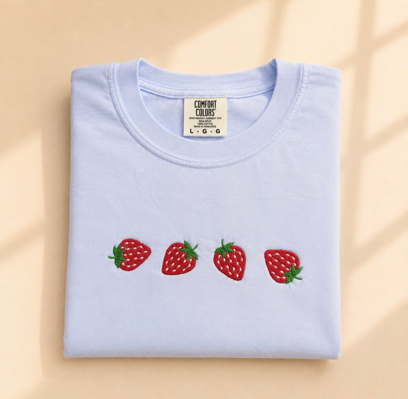 Light blue t-shirt with strawberry designs on a beige background