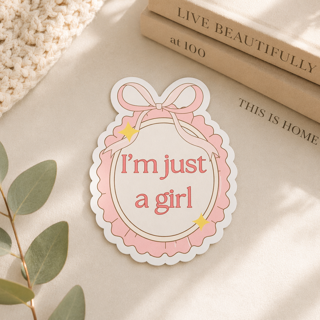 Sticker with 'I'm just a girl' text on a light surface with books and leaves.