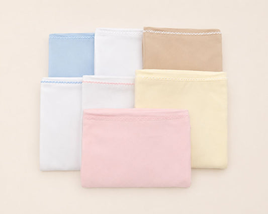Six folded fabric pouches or small cloth cases in pastel shades, including light blue, white, tan, pink, pale yellow, and white, arranged in two rows on a light beige background.