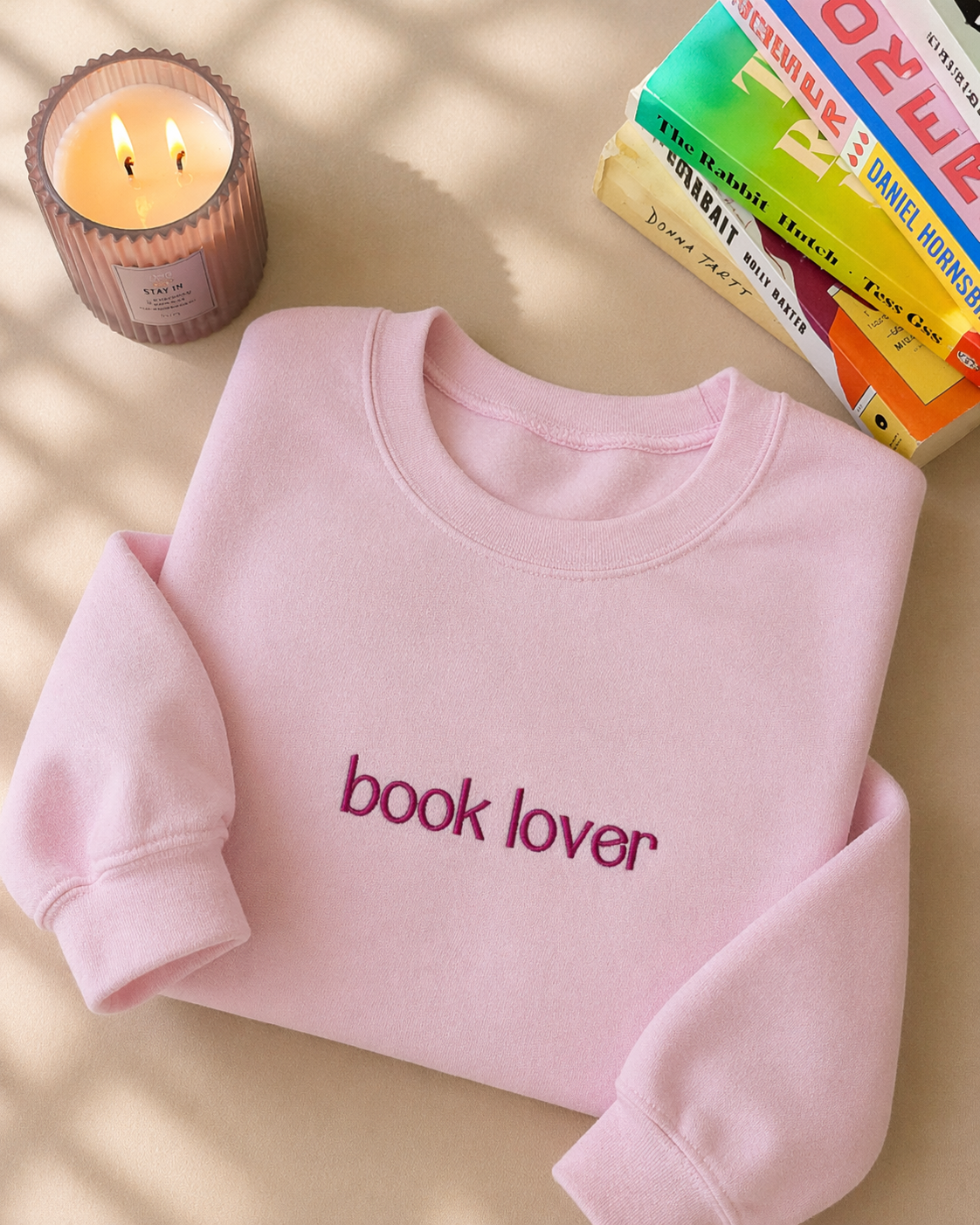 Pink sweatshirt with 'book lover' text on a surface with a candle and books.
