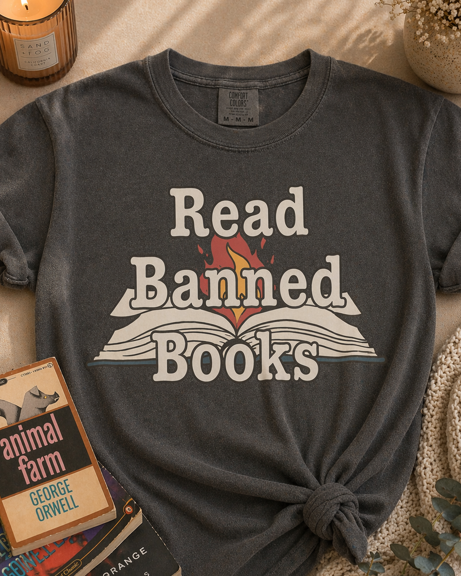 Dark gray t-shirt with 'Read Banned Books' text, placed on a surface with books and a candle.
