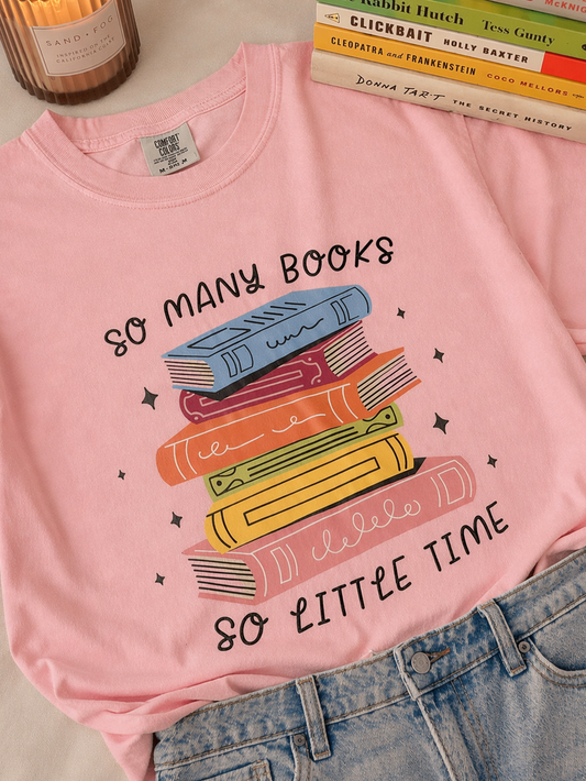 Pink t-shirt with book graphic and text, paired with books and a candle on a surface.