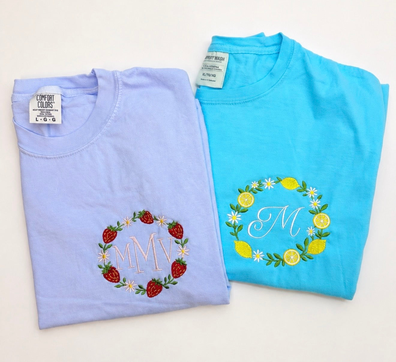 Flat lay of personalized embroidered Comfort Colors t-shirts featuring strawberry and lemon wreath designs with custom monograms embroidered in the center.