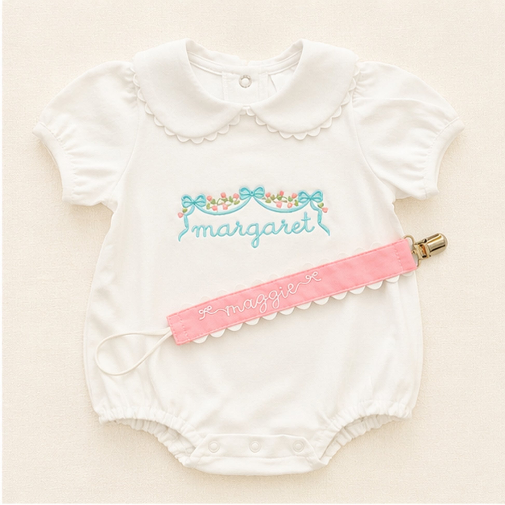 Personalized baby bubble romper with embroidered name and matching pink pacifier clip on ivory background
